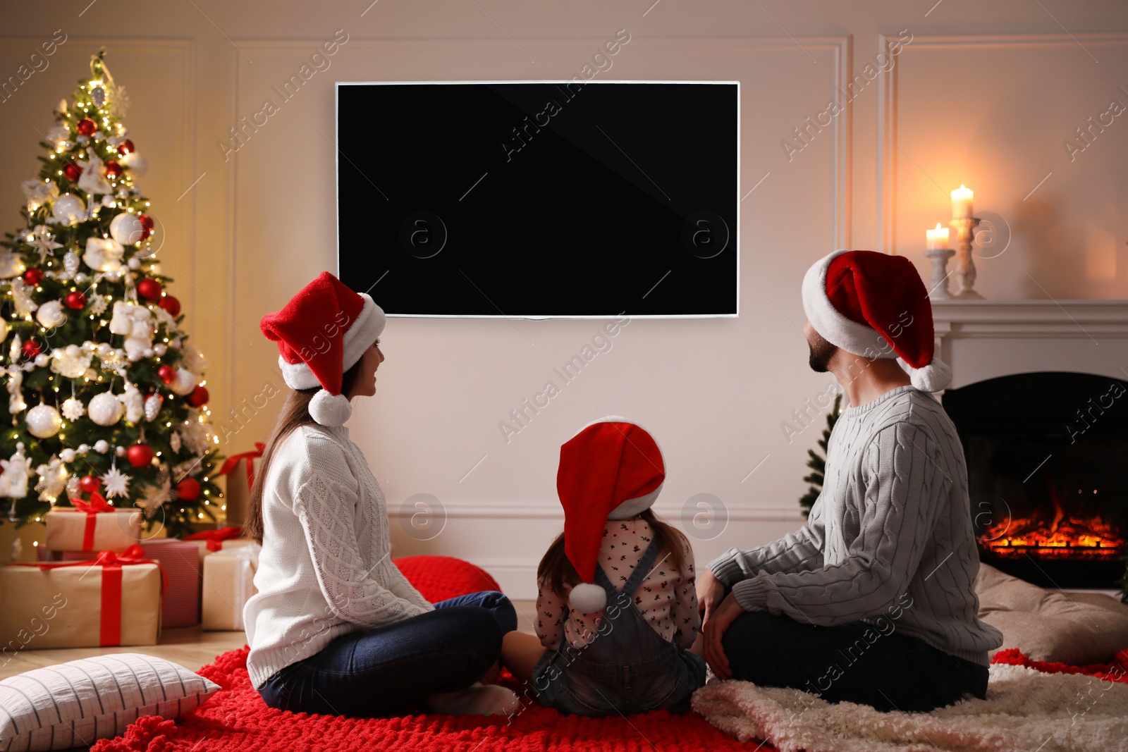 Image of Family watching TV in room decorated for Christmas