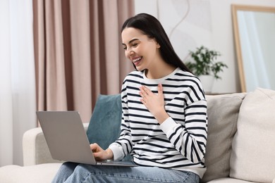 Happy young woman using laptop on sofa at home