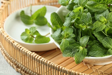 Photo of Bowl of fresh green mint leaves on wicker tray, closeup