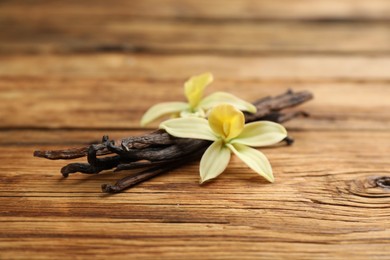 Photo of Aromatic vanilla sticks and flowers on wooden table, closeup