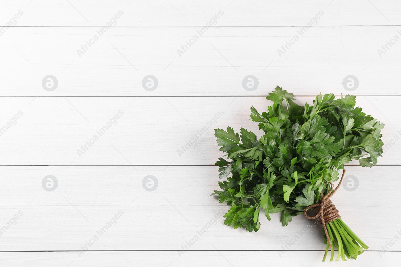 Photo of Bunch of fresh parsley on white wooden table, top view. Space for text
