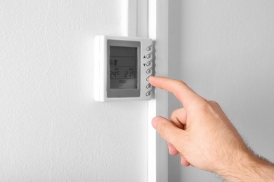 Photo of Man adjusting thermostat on white wall, closeup. Heating system