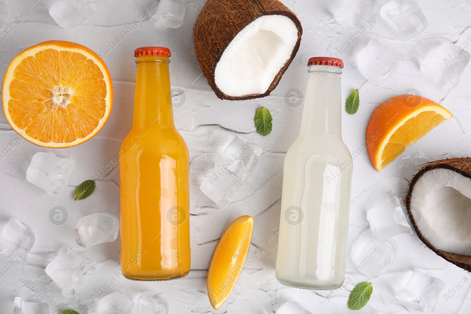 Photo of Tasty kombucha in glass bottles, fresh fruits and ice on white textured table, flat lay