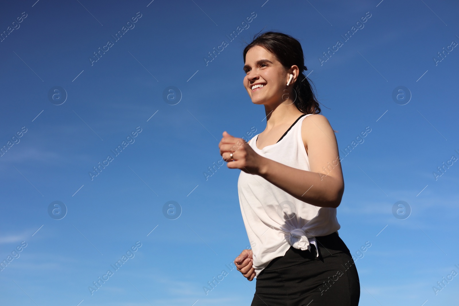 Photo of Young woman listening to music while running outdoors in morning, low angle view. Space for text