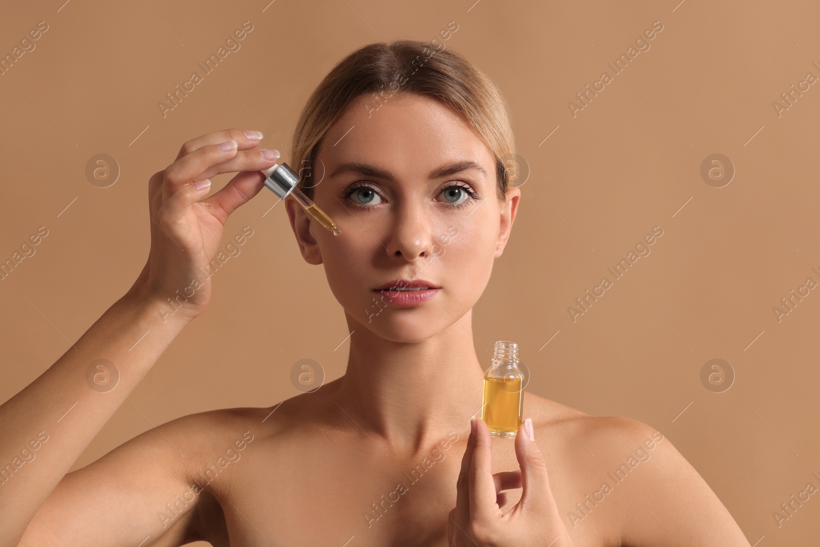 Photo of Beautiful woman applying cosmetic serum onto her face on beige background