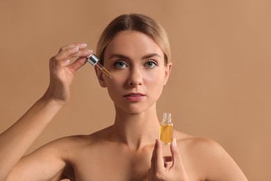 Beautiful woman applying cosmetic serum onto her face on beige background