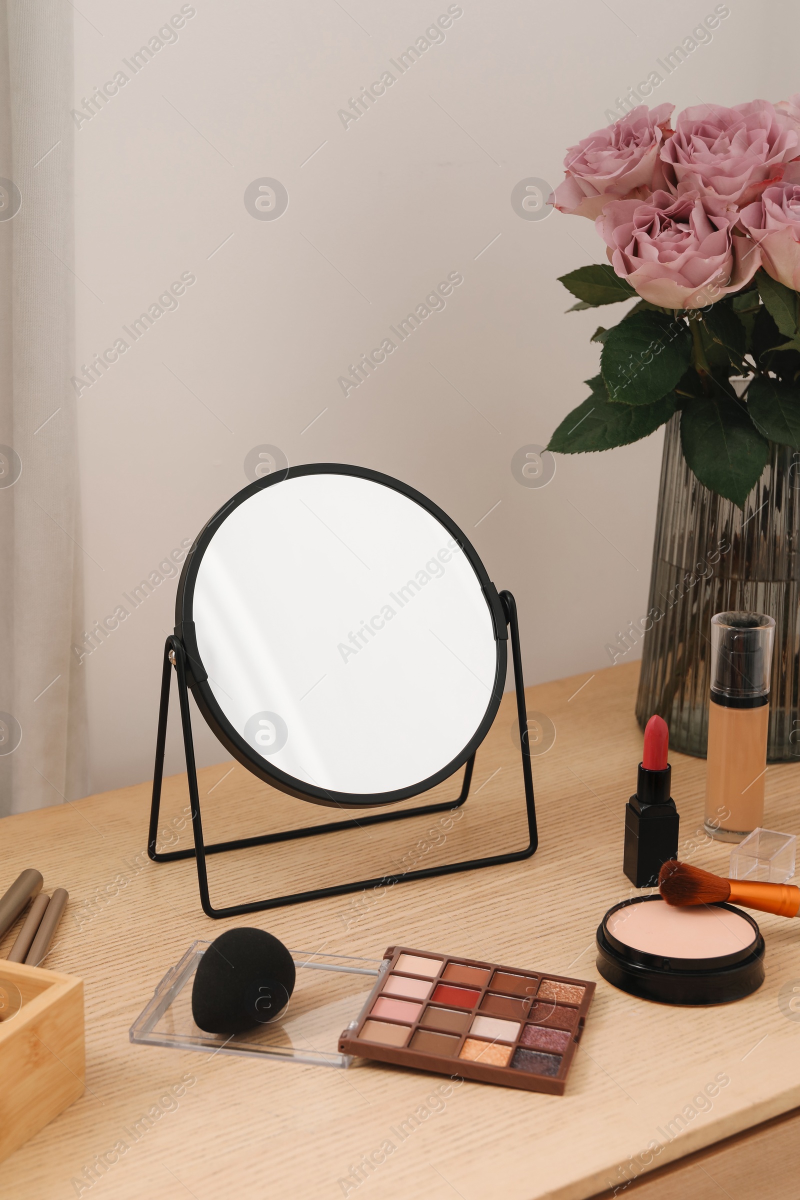 Photo of Mirror, cosmetic products and vase with pink roses on wooden dressing table in makeup room