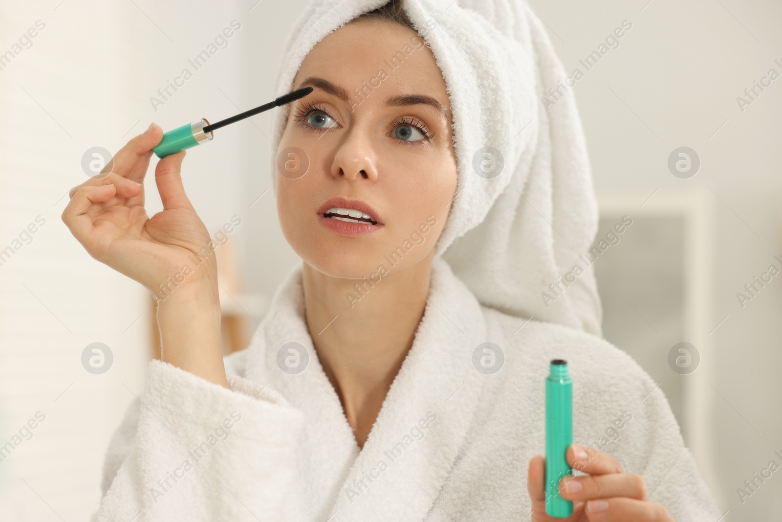 Photo of Beautiful woman applying mascara with brush indoors