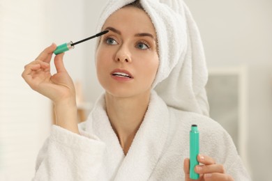 Photo of Beautiful woman applying mascara with brush indoors