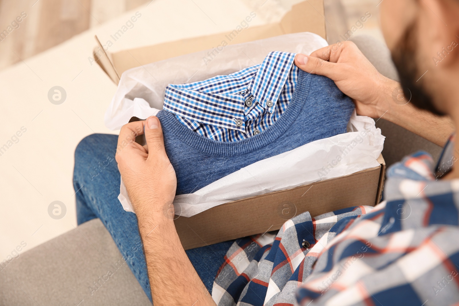 Photo of Young man opening parcel at home, closeup