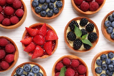 Photo of Tartlets with different fresh berries on white wooden table, flat lay. Delicious dessert