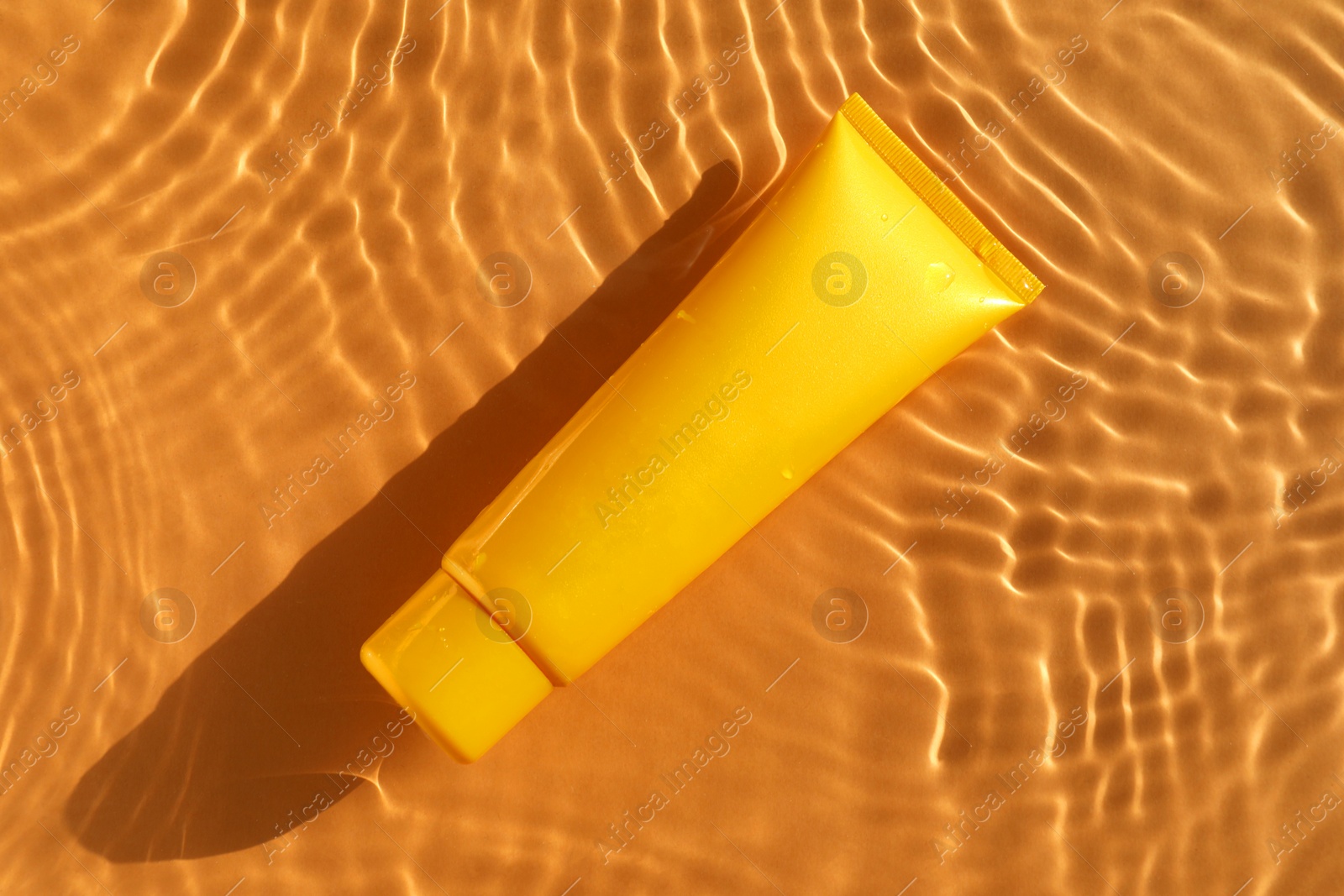 Photo of Tube with moisturizing cream in water on orange background, top view