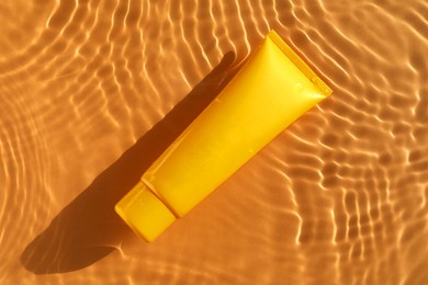 Tube with moisturizing cream in water on orange background, top view