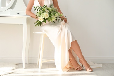 Young bride wearing wedding dress with beautiful bouquet in room, closeup