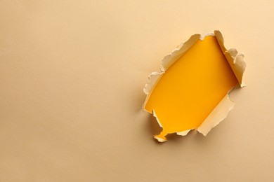 Photo of Hole in light beige paper on yellow background, space for text