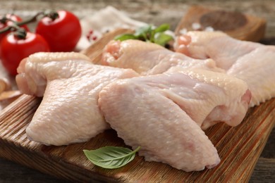 Photo of Raw chicken wings with basil on wooden board, closeup