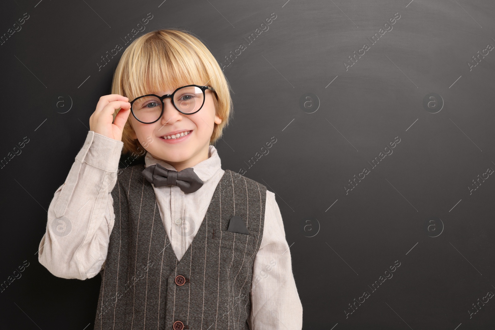 Photo of Happy little school child in uniform near chalkboard. Space for text