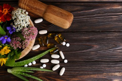 Photo of Mortar with fresh herbs, flowers and pills on wooden table, flat lay. Space for text