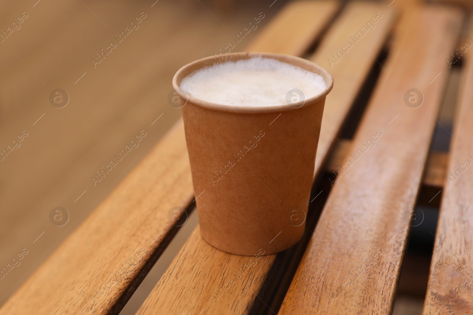 Photo of Takeaway paper cup with coffee on wooden table, closeup