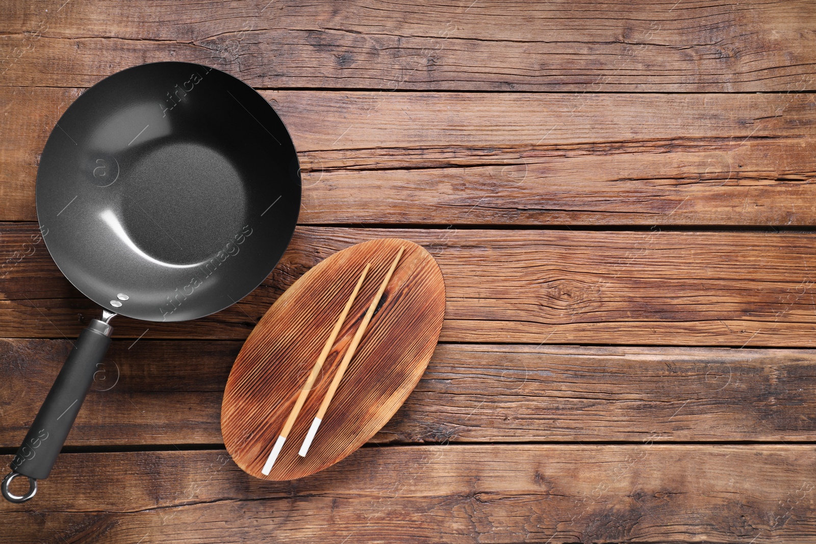 Photo of Empty iron wok and chopsticks on wooden table, flat lay. Space for text
