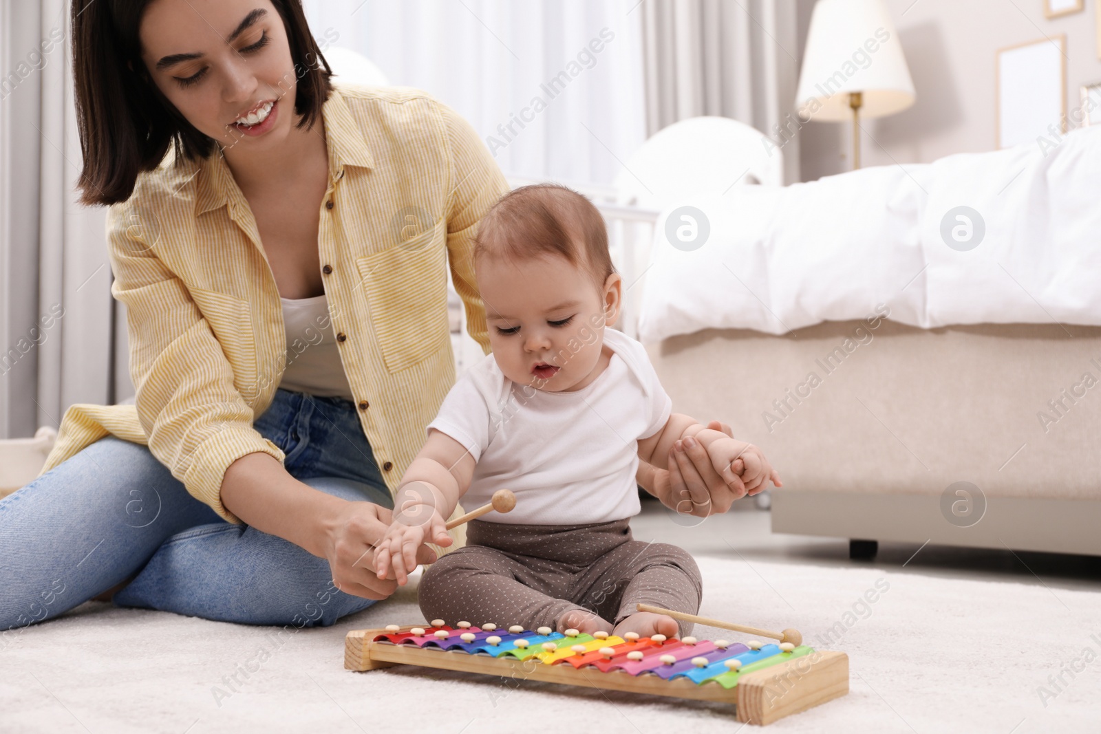 Photo of Cute baby and mother playing with xylophone on floor at home