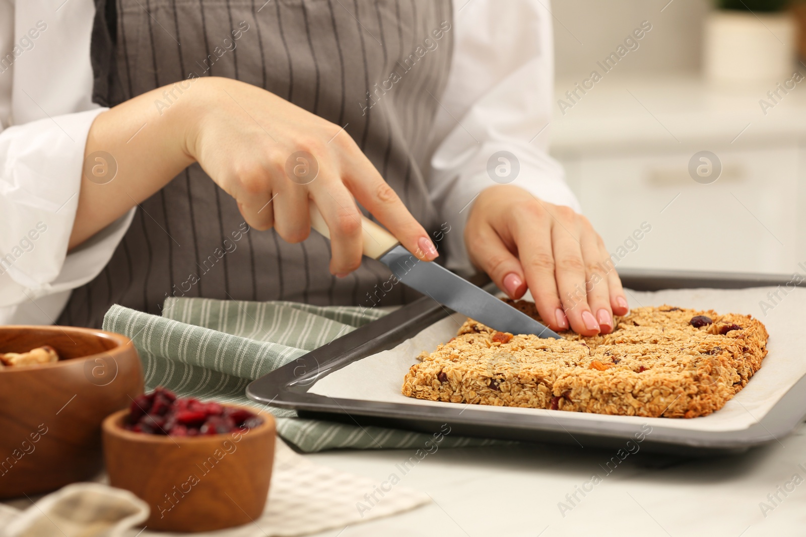 Photo of Woman cutting granola bars at table in kitchen, closeup