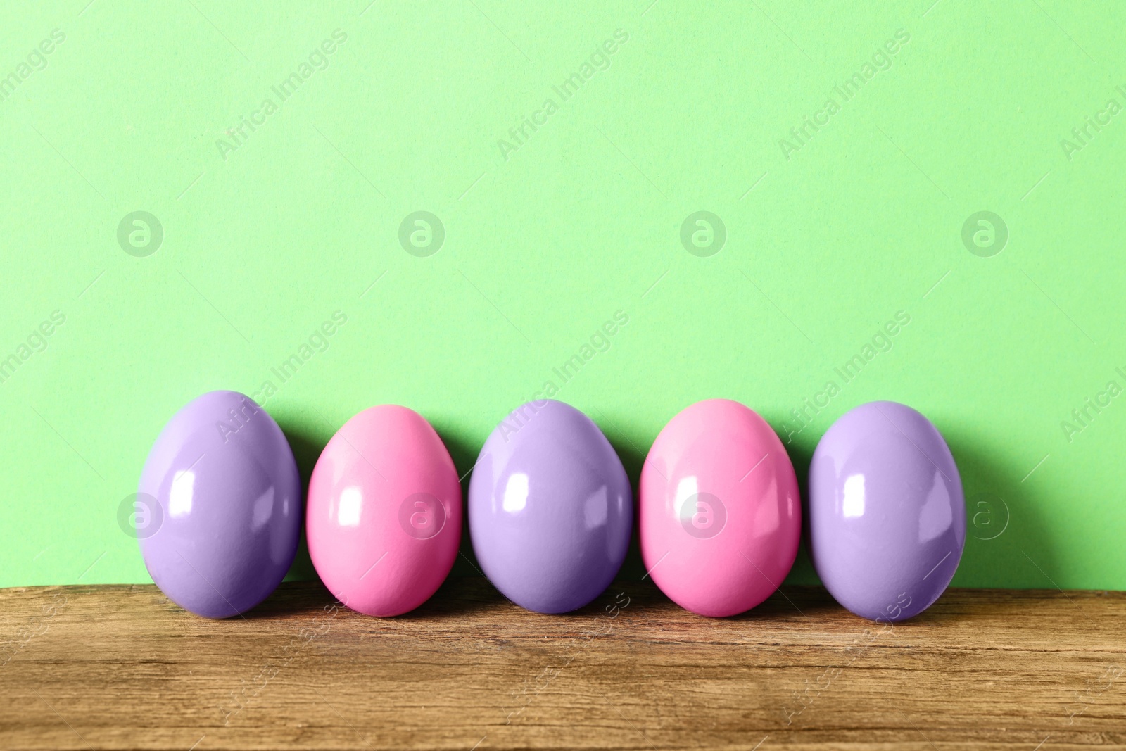 Photo of Easter eggs on wooden table against green background, space for text