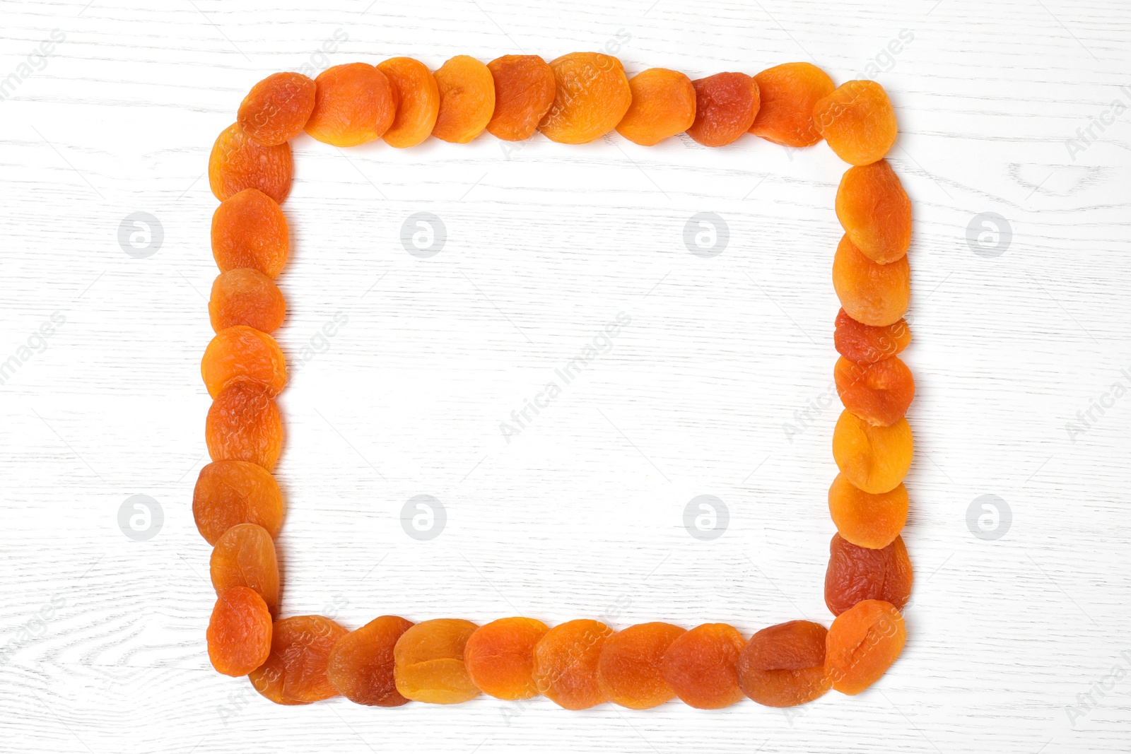 Photo of Frame made of dried apricots on white wooden table, top view with space for text. Healthy fruit