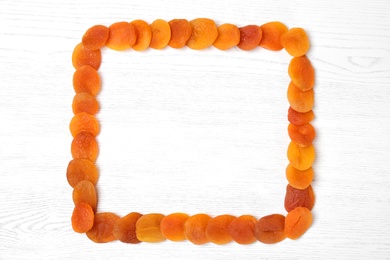 Photo of Frame made of dried apricots on white wooden table, top view with space for text. Healthy fruit