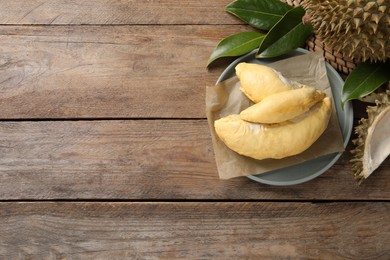 Photo of Fresh ripe durians and leaves on wooden table, flat lay. Space for text