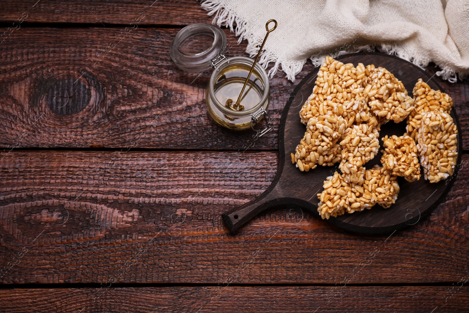 Photo of Board with puffed rice bars (kozinaki) on wooden table, flat lay. Space for text