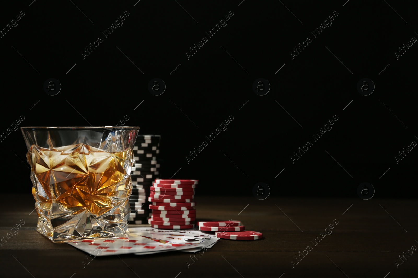 Photo of Casino chips, playing cards and glass of whiskey on wooden table, space for text