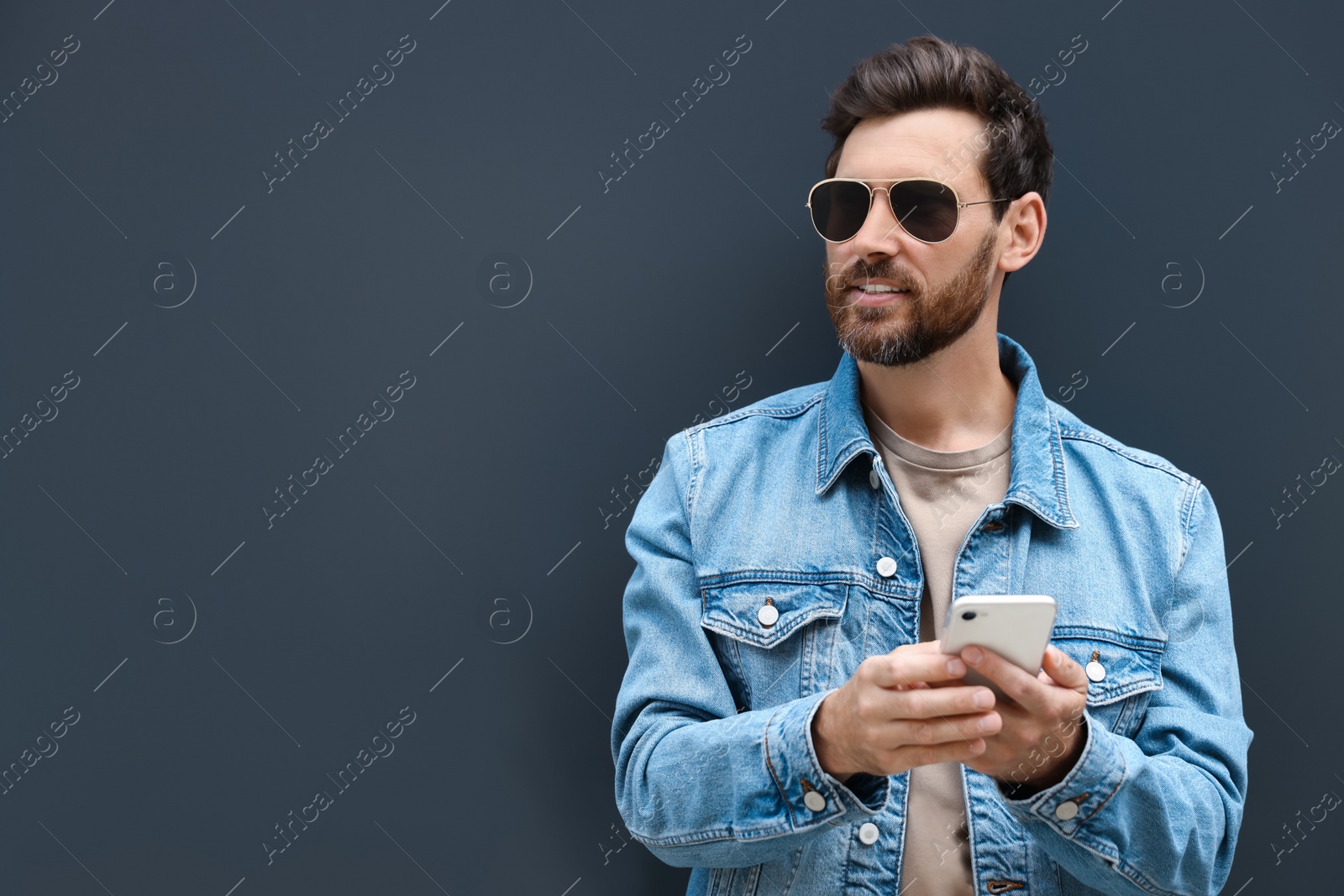 Photo of Handsome bearded man with smartphone near grey wall outdoors. Space for text