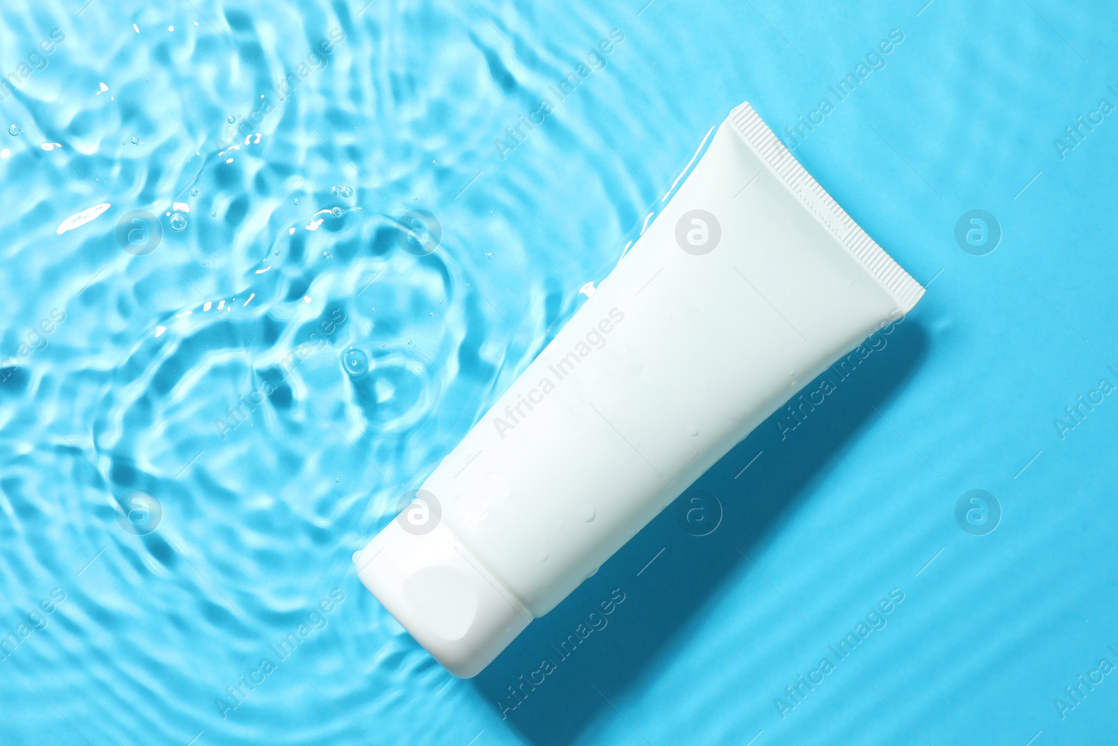 Photo of Tube with moisturizing cream in water on light blue background, top view