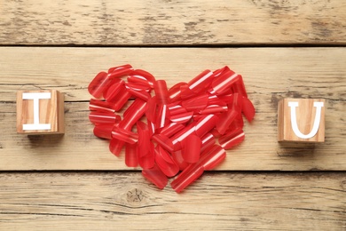 Photo of Red confetti in shape of heart and cubes with letters forming phrase I Love You on wooden background, flat lay