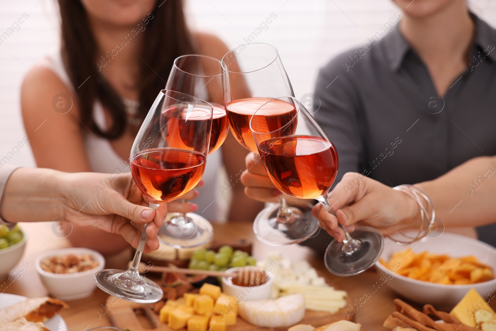 Photo of People clinking glasses with rose wine above wooden table indoors, closeup