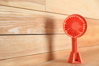 Portable fan on table near wooden wall, space for text. Summer heat