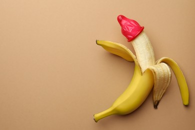 Photo of Banana with condom on pale orange background, top view and space for text. Safe sex concept