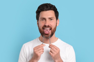 Happy man brushing his tongue with cleaner on light blue background