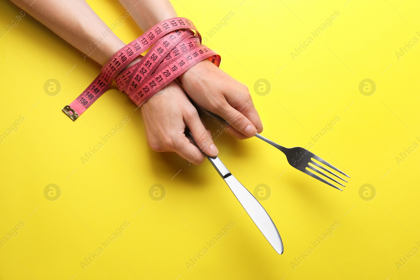 Photo of Woman with tied hands holding cutlery on yellow background, top view. Diet concept