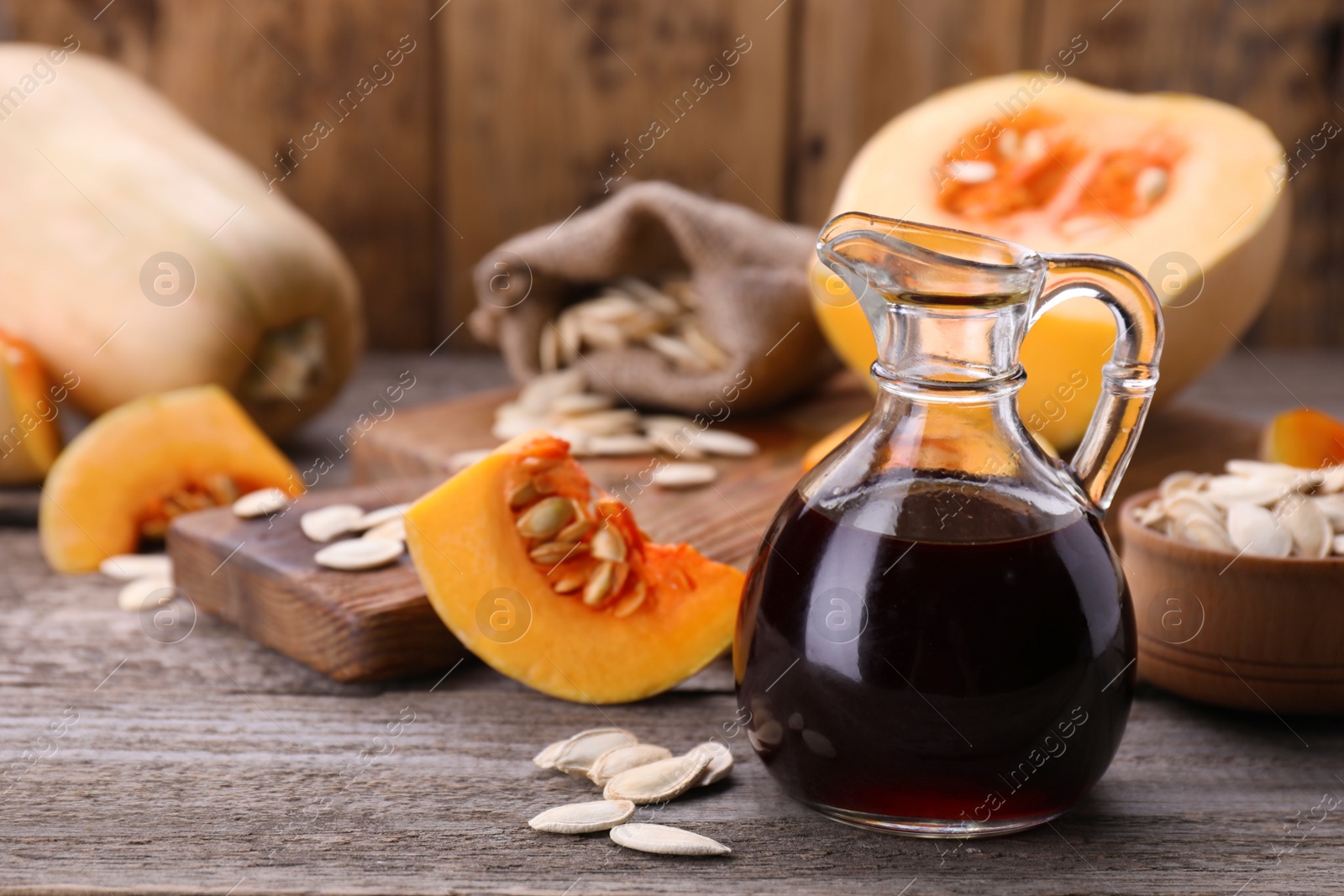 Photo of Fresh pumpkin seed oil in glass jug on wooden table. Space for text