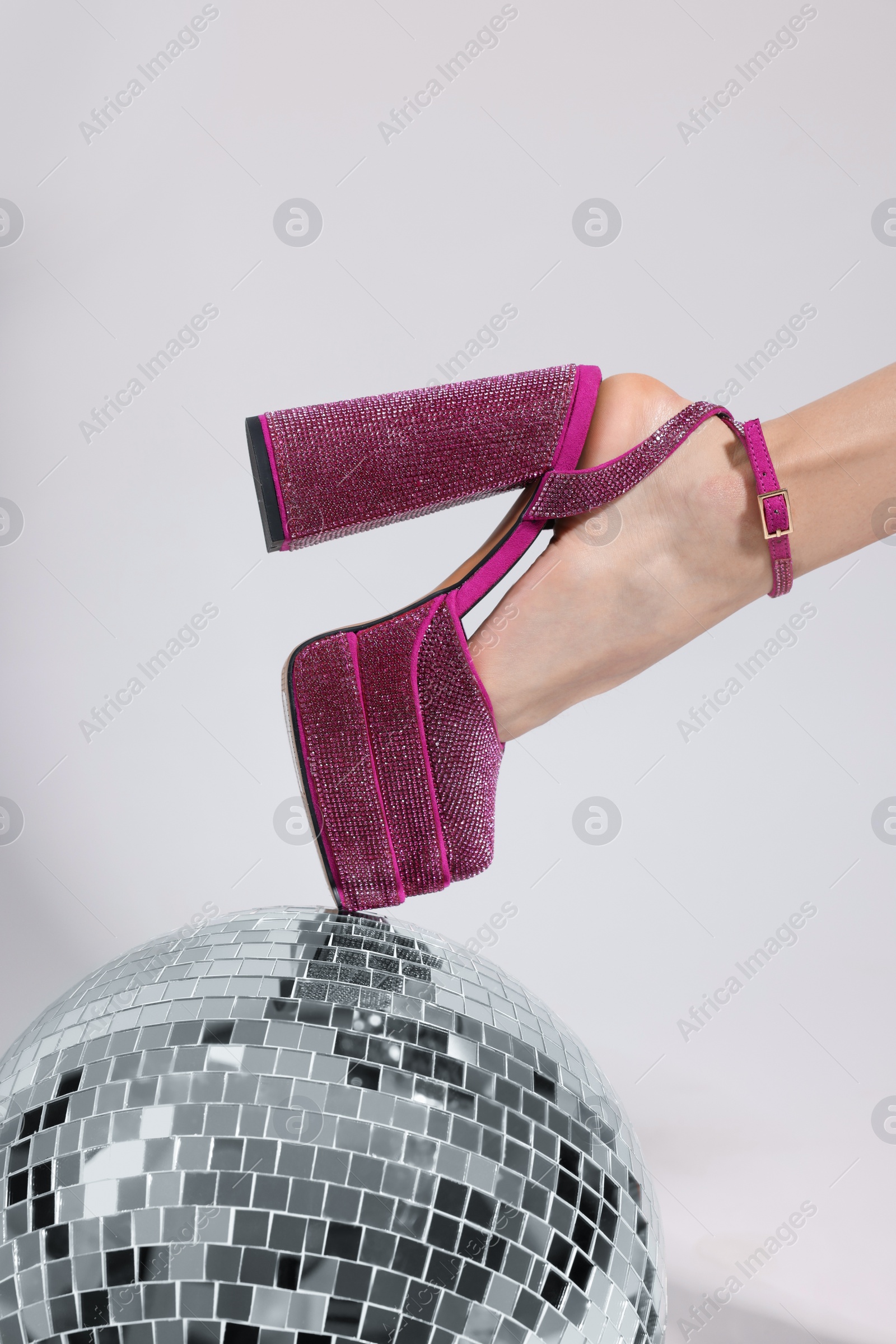 Photo of Stylish woman in pink high heeled shoes and disco ball on white background, closeup