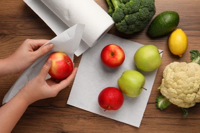 Photo of Woman wiping apple with paper towel at wooden table, top view