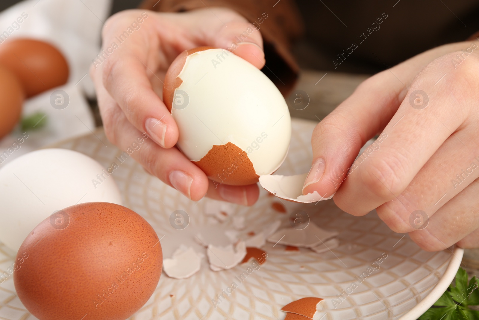 Photo of Woman peeling boiled egg over plate, closeup