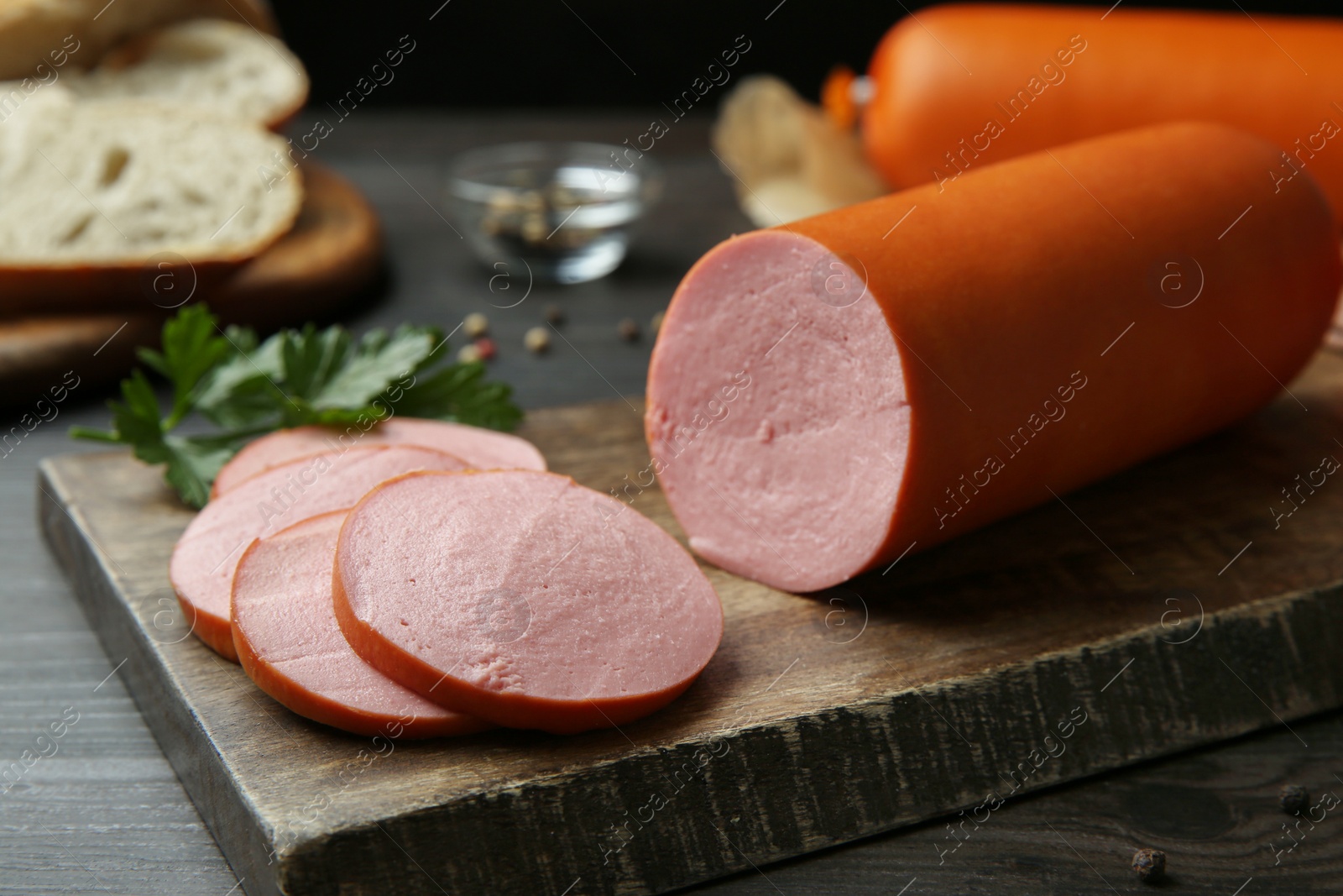 Photo of Board with tasty boiled sausage on dark wooden table, closeup