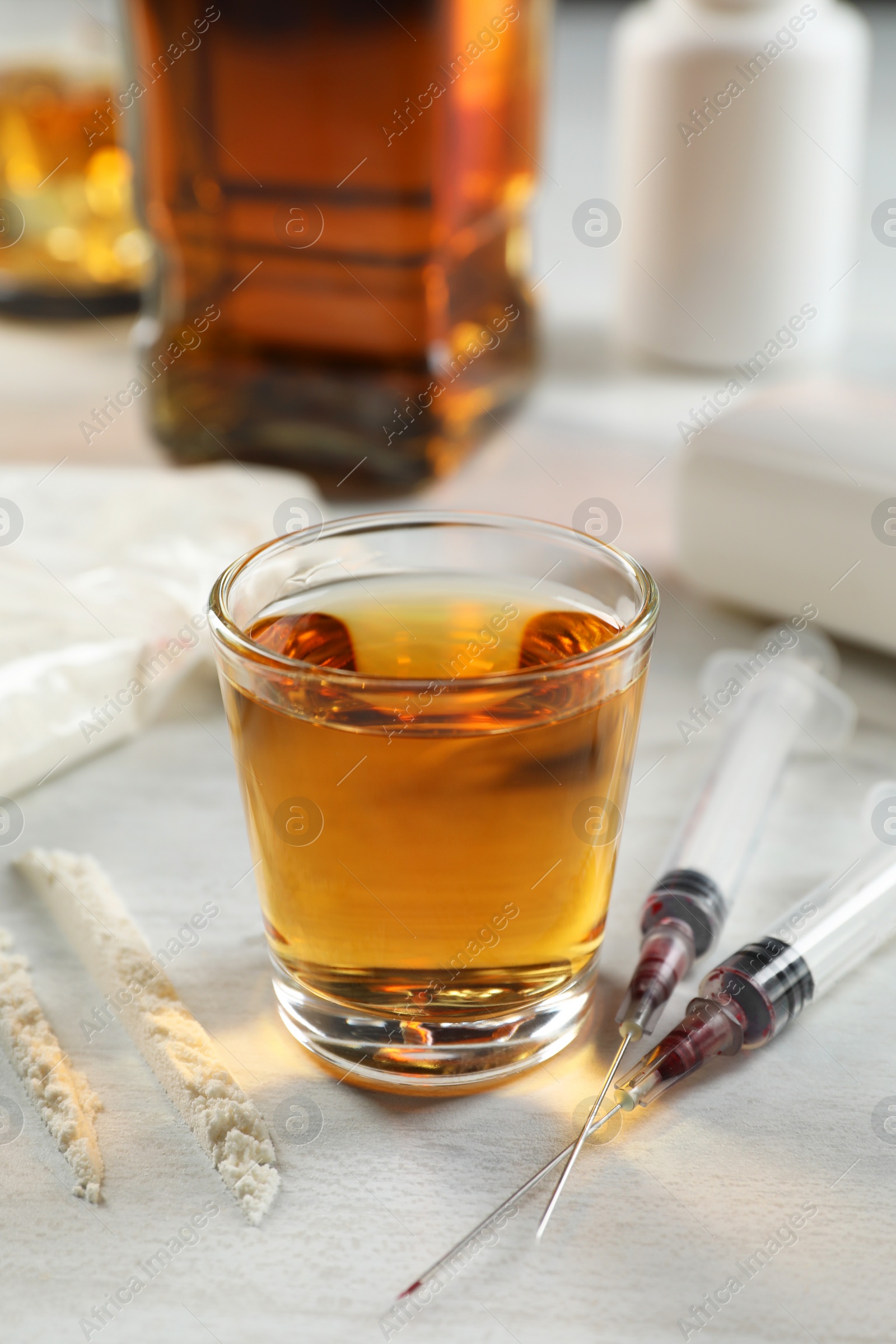 Photo of Alcohol and drug addiction. Whiskey in glass, syringes and cocaine on white table