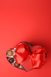 Photo of Heart shaped box with delicious chocolate candies on red table, top view. Space for text
