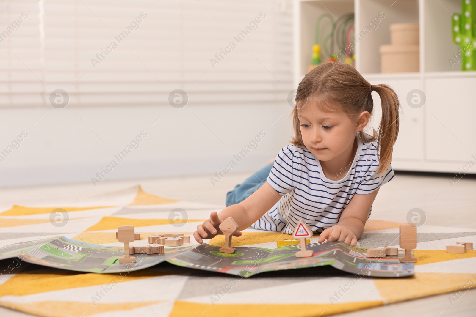 Photo of Cute little girl playing with set of wooden road signs and cars indoors, space for text. Child's toy