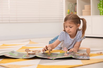 Photo of Cute little girl playing with set of wooden road signs and cars indoors, space for text. Child's toy