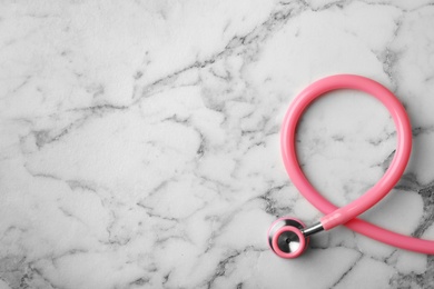 Photo of Pink stethoscope folded like awareness ribbon on marble background, top view with space for text. Breast cancer concept